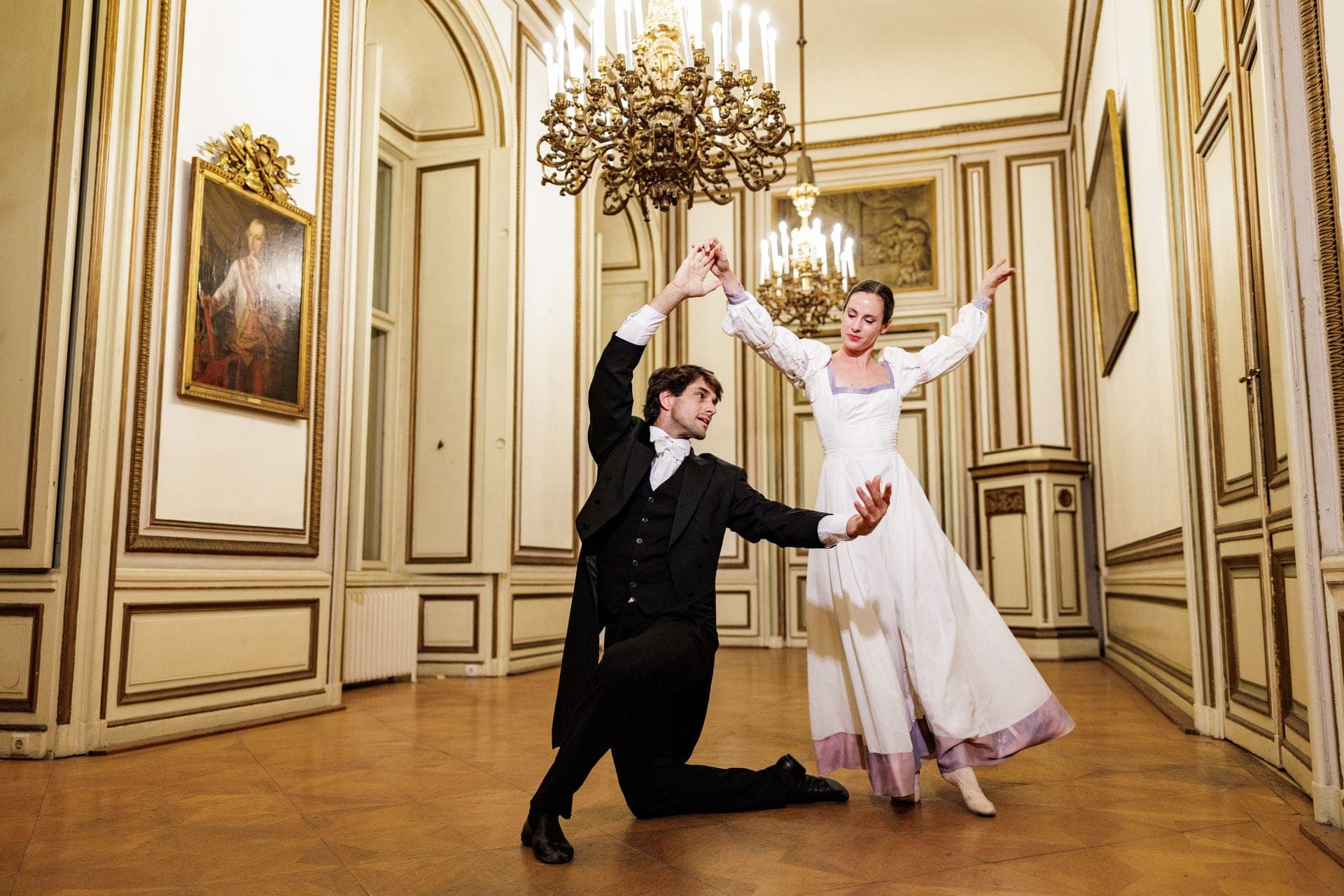Two dancers in historical costume in a white-and-gold salon