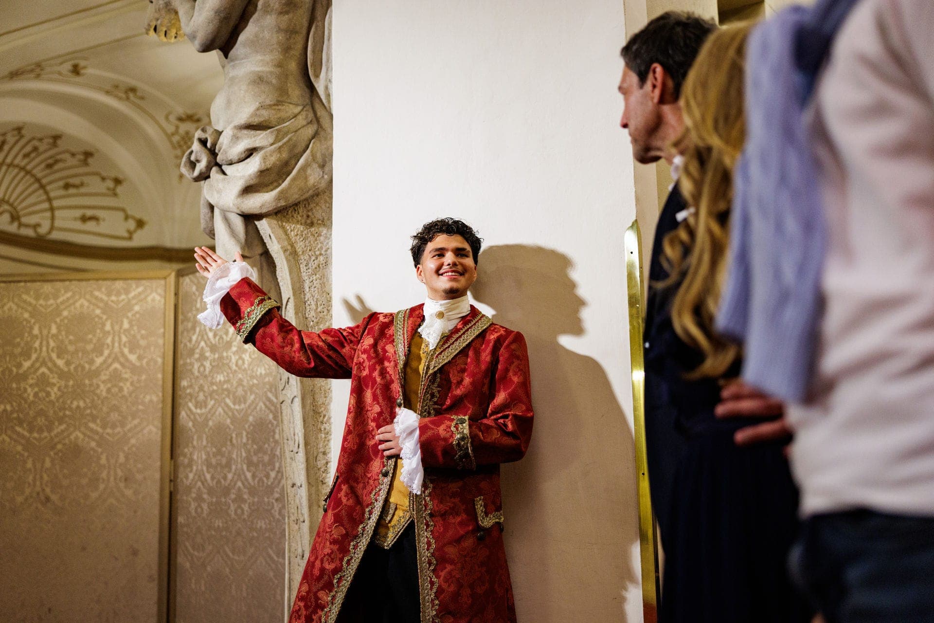 Host in a red 18th-century costume welcoming guests