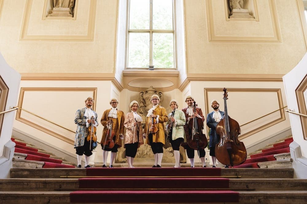 Orchestra members in period costume with their instruments on the grand staircase
