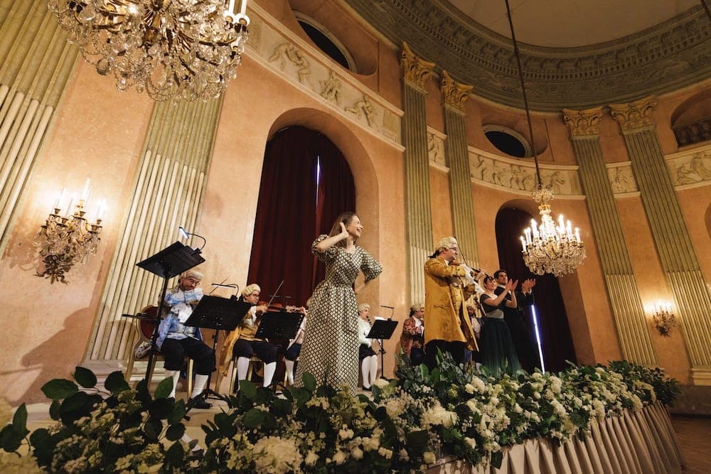Singer and costumed orchestra on the flower-lined stage of the columned hall