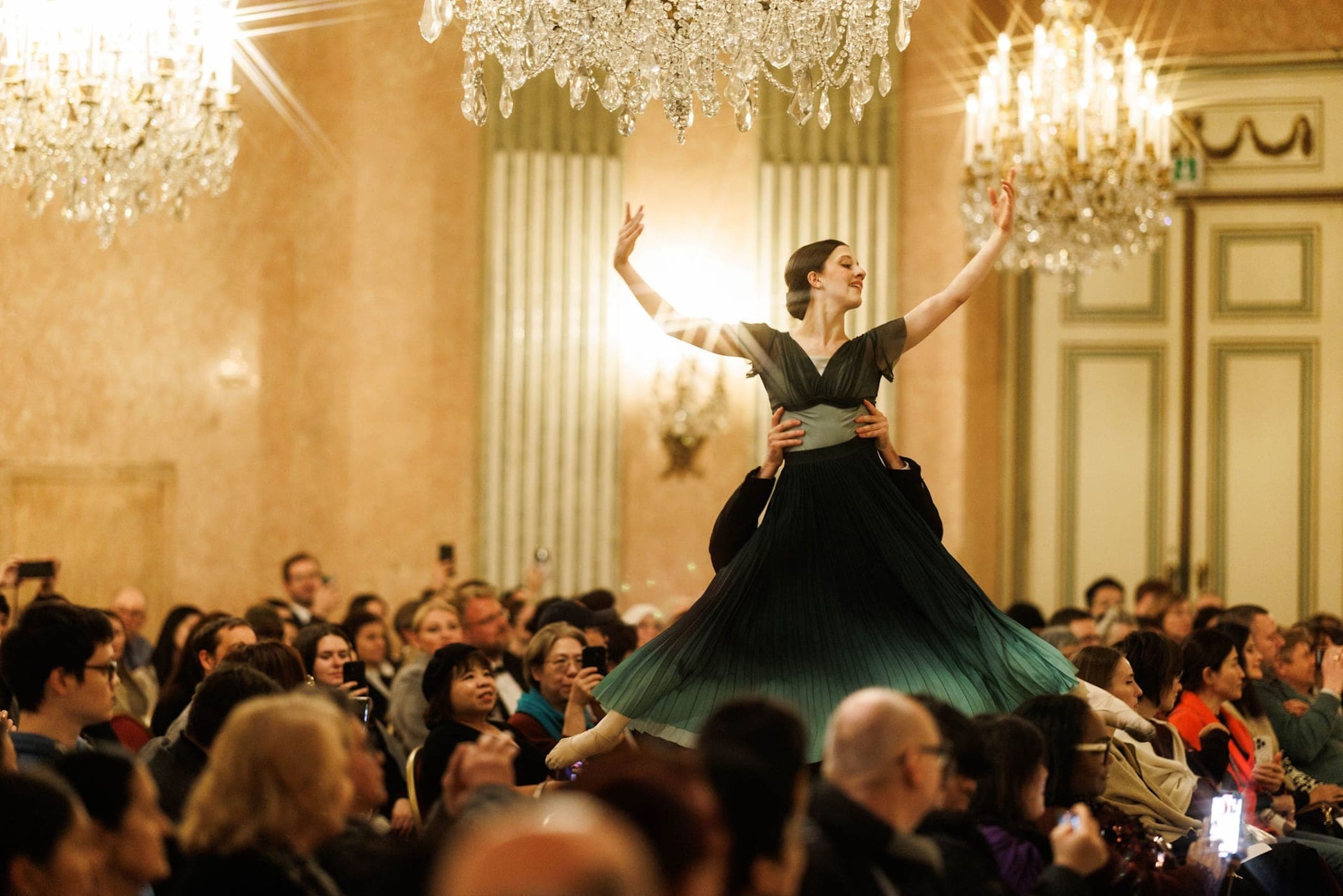 Ballerina in a green dress lifted by her partner before a full audience