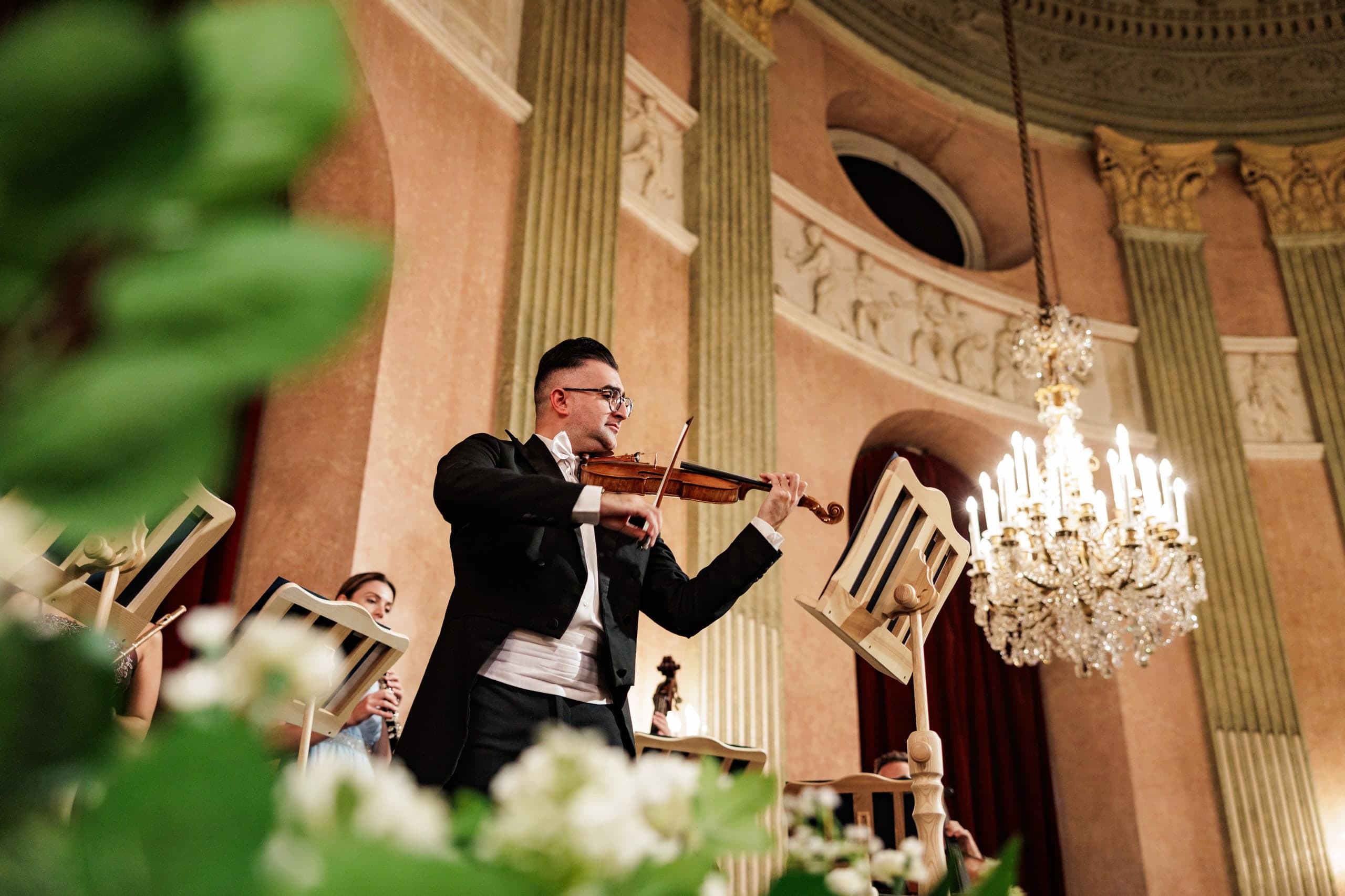 Violinist in a tailcoat playing under a chandelier, flowers in the foreground
