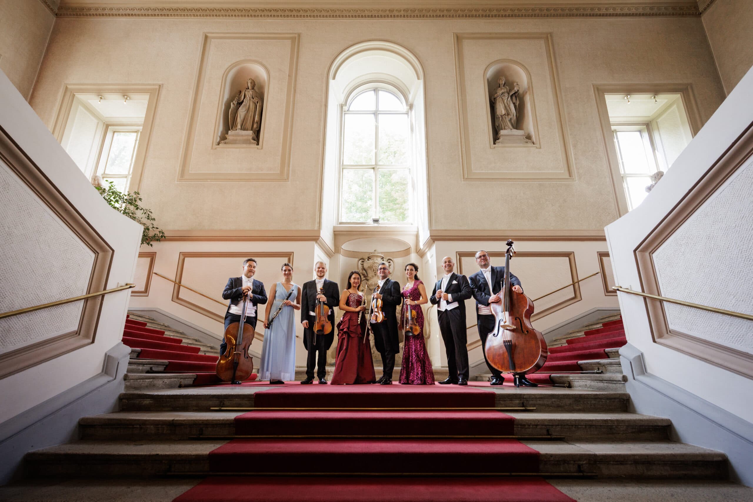 Musicians and singers with their instruments posing on the red-carpeted staircase