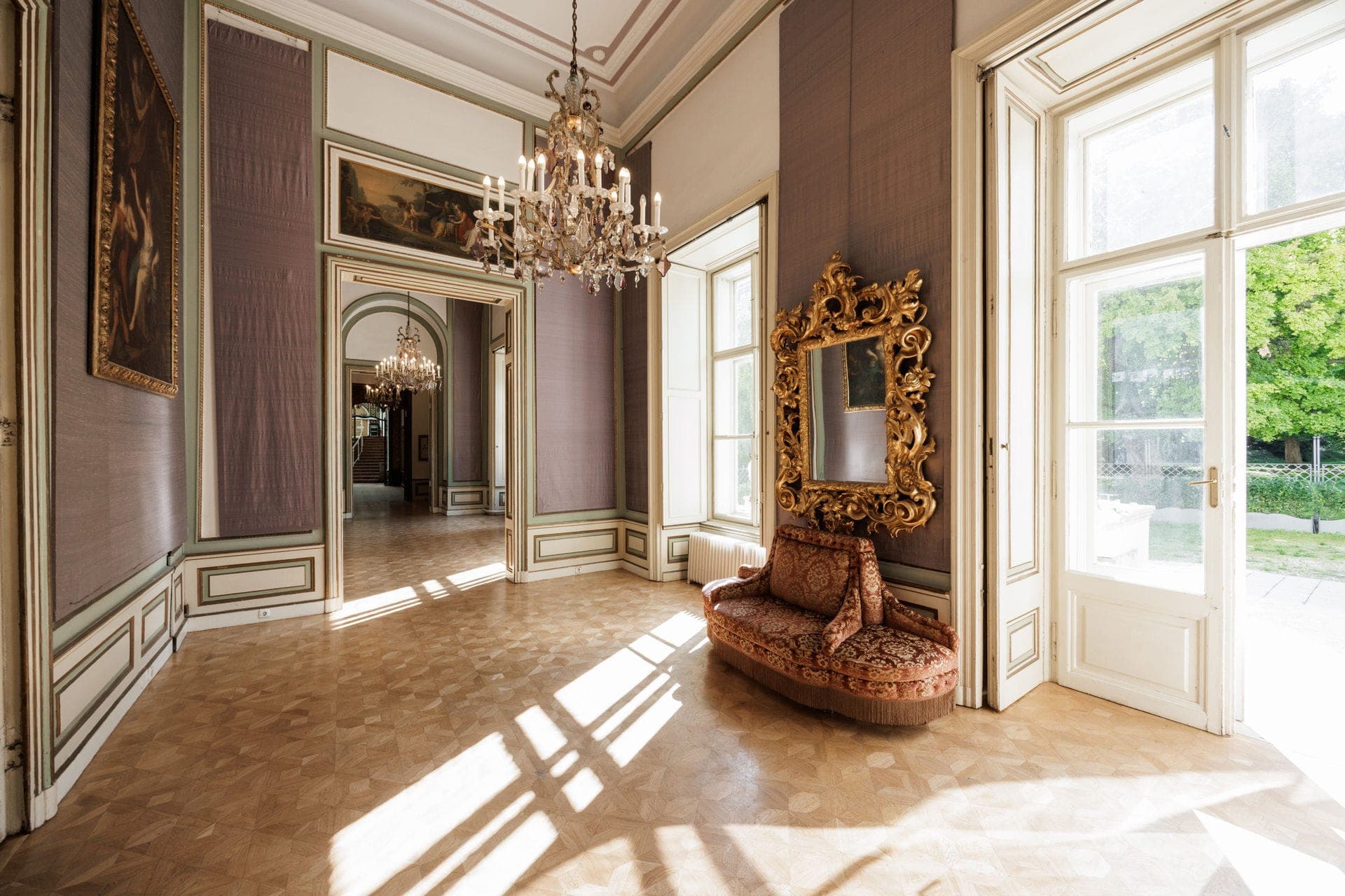 Sunlit salon with chandelier, gilded mirror, parquet floor and garden doors