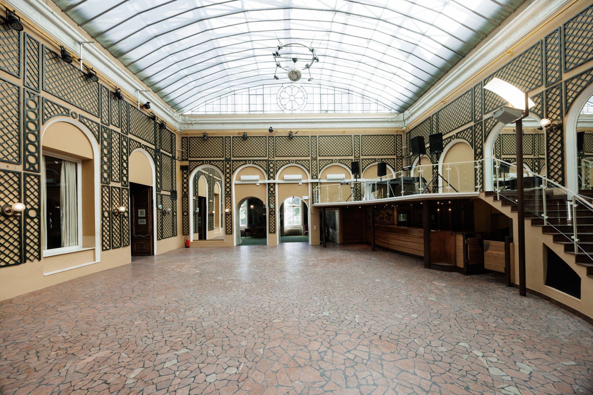 Glass-roofed hall with trellised walls and a gallery staircase
