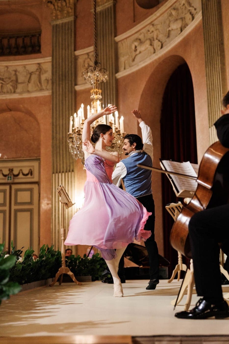 Ballet couple, she in a pink dress, dancing beside a cellist