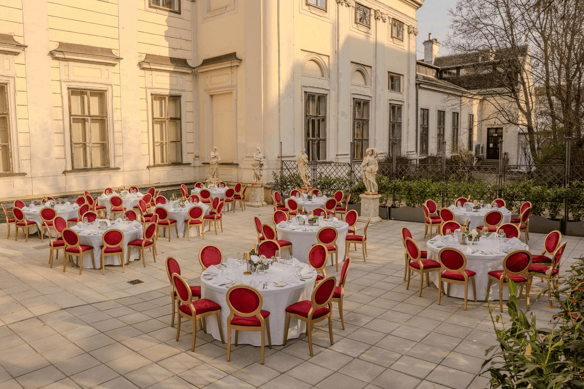 Palace courtyard terrace with round dinner tables, red-gold chairs and statues