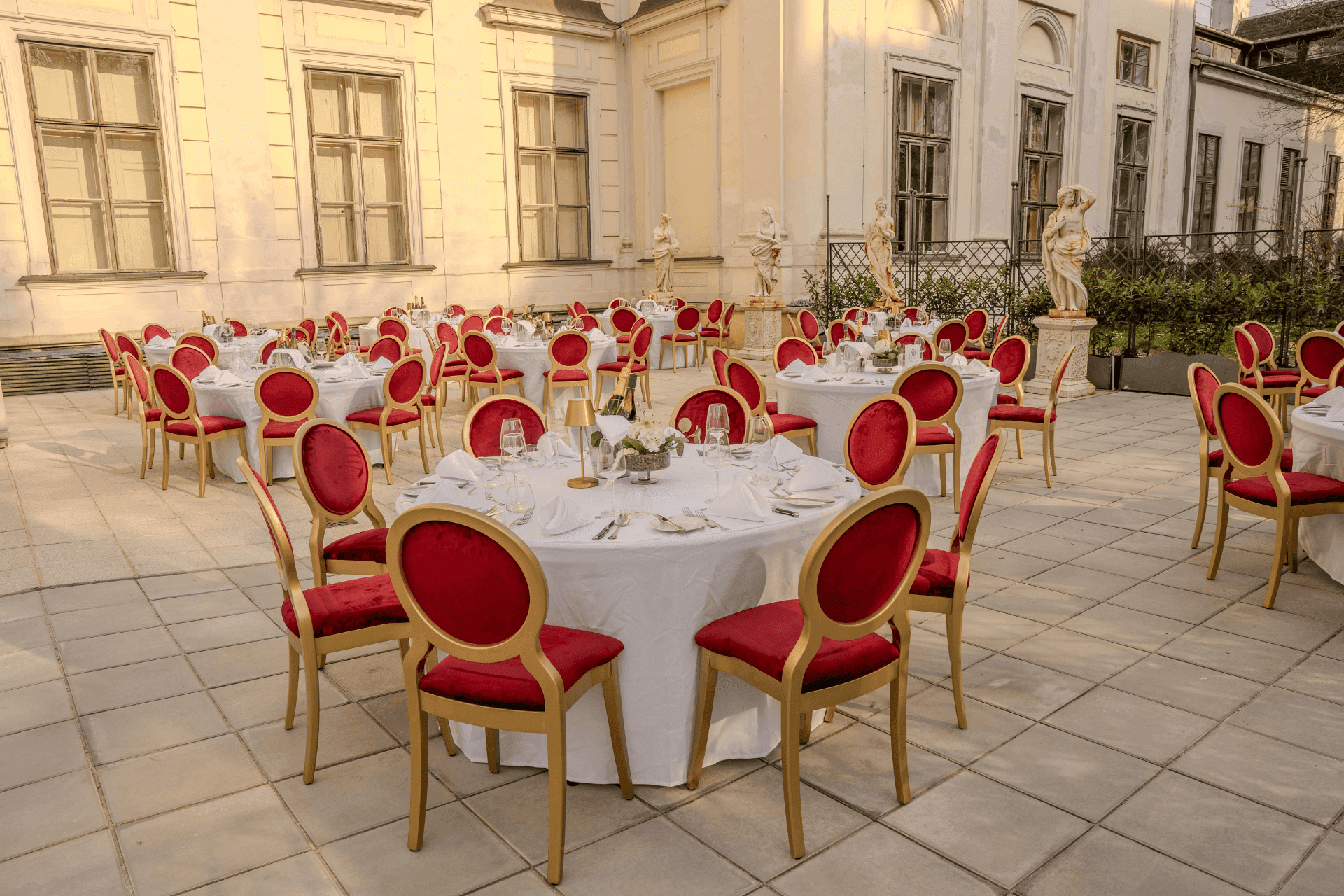 Palace courtyard terrace with round dinner tables, red-gold chairs and statues