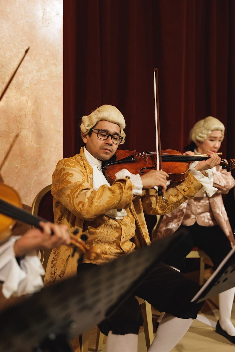 Violinist in a gold brocade costume and wig playing in the orchestra