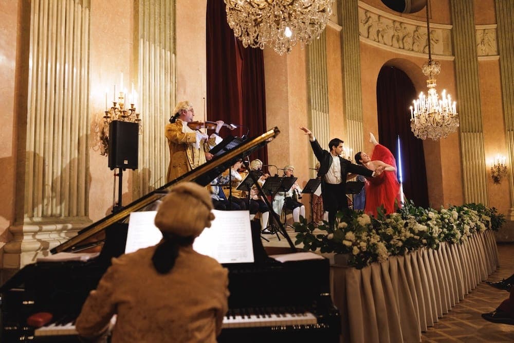 View past the pianist to the stage, where a ballet couple dances with the orchestra