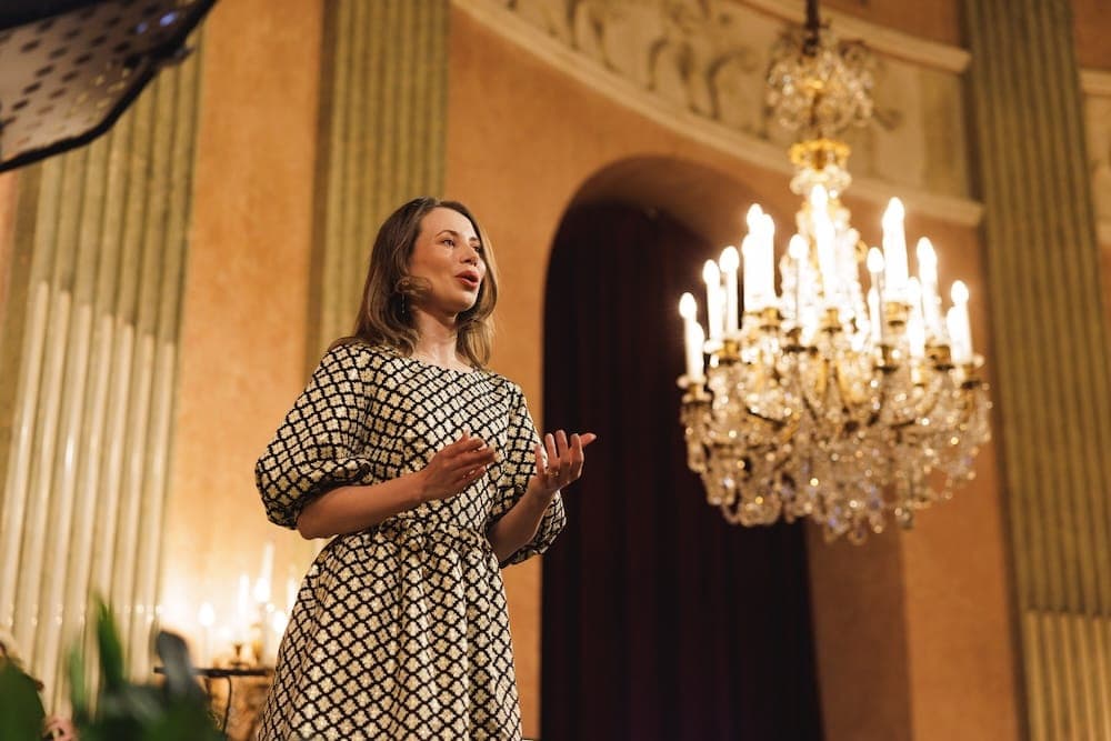 Singer in a patterned dress performing beneath a crystal chandelier