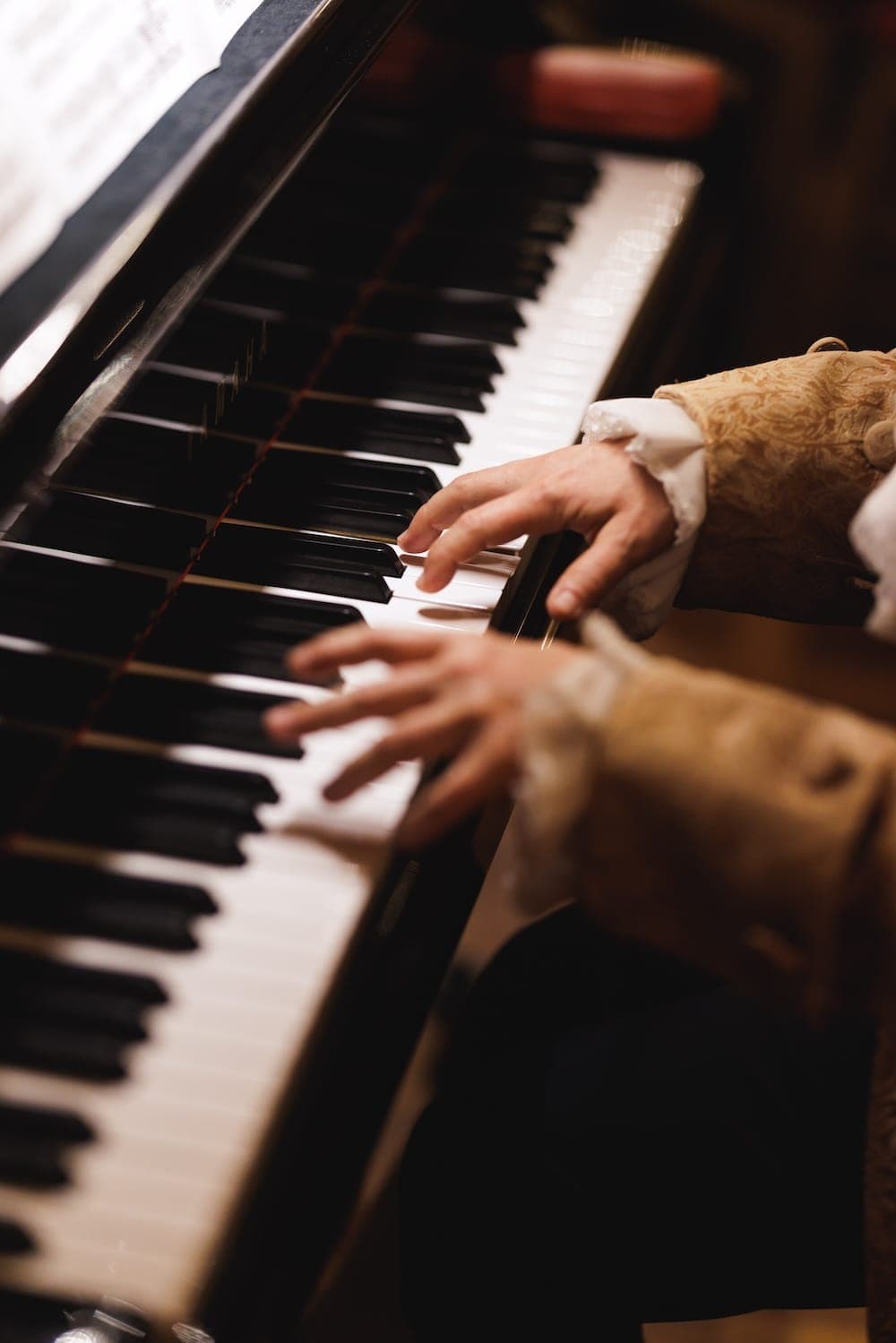 Close-up of hands in a period-costume sleeve on piano keys