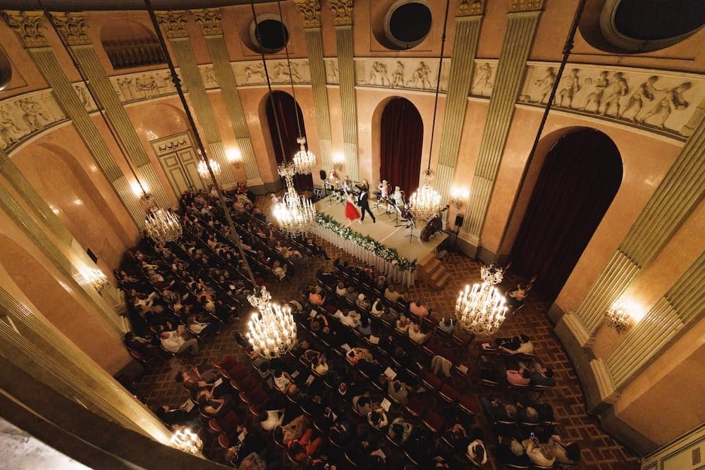Full concert hall seen from the gallery, with chandeliers and stage